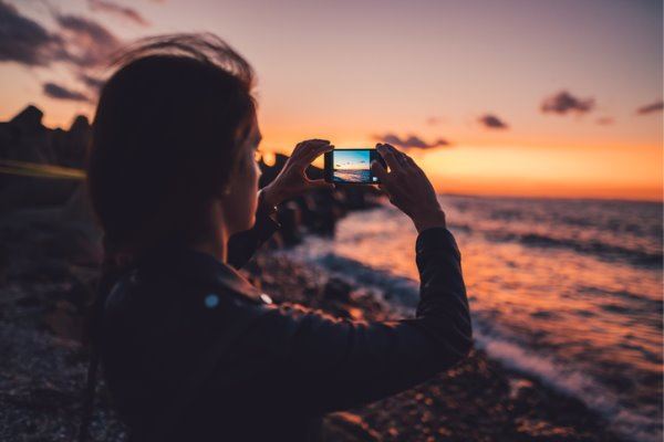 woman-at-the-beach-photographing-the-sunset-picture-id929516304